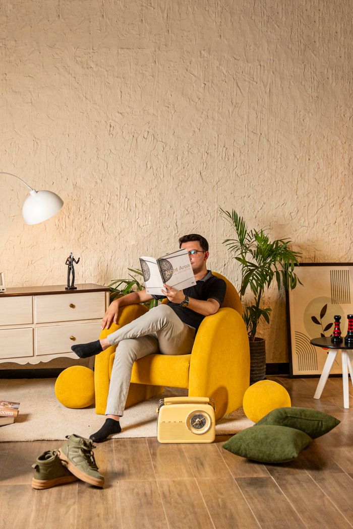 services-01 Man reads a magazine in a stylish living room with a yellow chair and vintage decor.